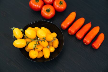 Top view of yellow and red cherry tomatoes in bowl on black wooden backgroundの写真素材