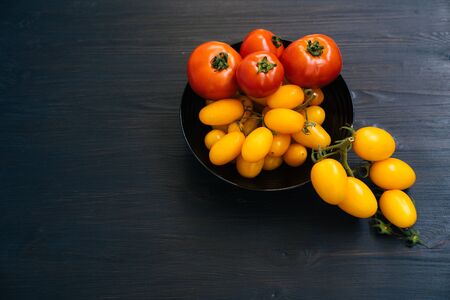 Top view of yellow and red cherry tomatoes in bowl on black wooden backgroundの写真素材
