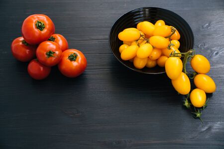 Top view of yellow and red cherry tomatoes in bowl on black wooden backgroundの写真素材