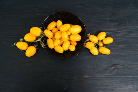 Top view of yellow cherry tomatoes in bowl on black wooden background with copy space. Concept of vegetableの写真素材