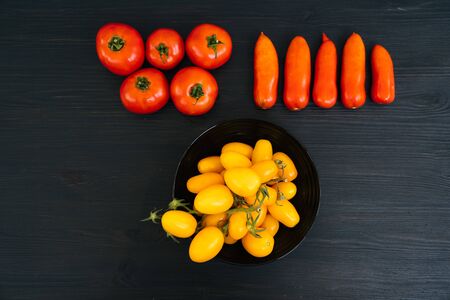 Top view of yellow and red cherry tomatoes in bowl on black wooden background with copy space. Concept of vegetableの写真素材