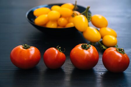 Top view of yellow and red cherry tomatoes in bowl on black wooden background. Concept of vegetableの写真素材