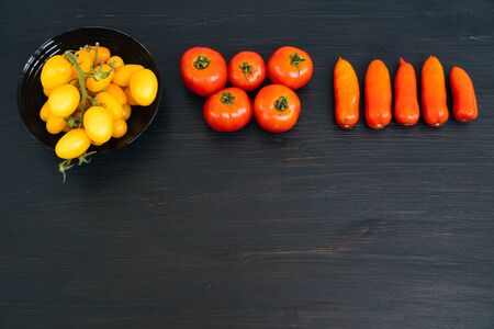 Top view of yellow and red cherry tomatoes in bowl on black wooden background with copy space. Concept of vegetableの写真素材