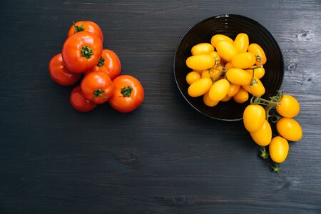 Top view of yellow and red cherry tomatoes in bowl on black wooden backgroundの写真素材