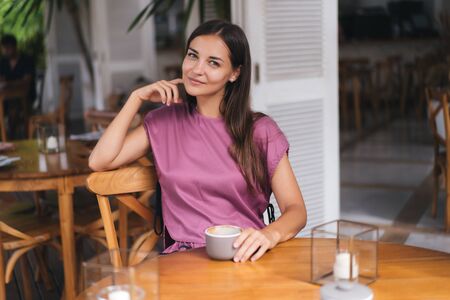 Portrait of beautiful woman drinking hot beverage from cup in cafe and smilingの写真素材
