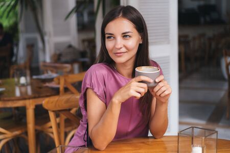 Portrait of beautiful woman drinking hot beverage from cup in cafe and smilingの写真素材