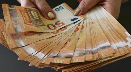 Woman shows a stack of money of 50 euro banknotes on a gray background. Woman holds euro money in...