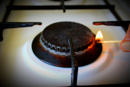 A woman lights a gas burner of a stove with a matchstick in the kitchen close up. View from an angle.の写真素材