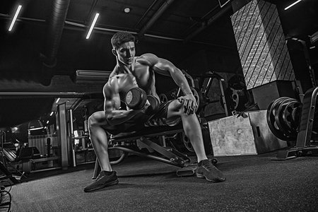 In the gym, the Asian man does exercises on the fitness bench, heavy training of hands, biceps,...