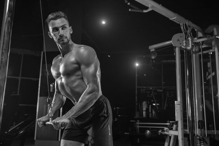 Muscular bodybuilder guy doing exercises with dumbbells in gym