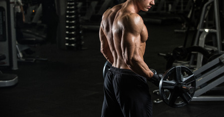 young muscular man exercising with dumbbells. Guy trains his bicepの写真素材