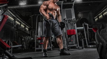 Close up of young muscular man lifting weights over dark backgroundの写真素材
