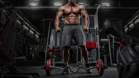 Close up of young muscular man lifting weights over dark backgroundの写真素材