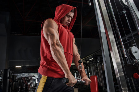 Muscular athletic bodybuilder man hard workout in gym over dark background with dramatic light with...