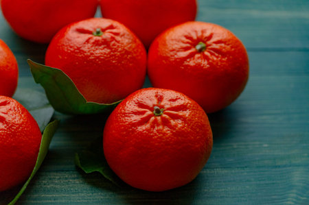 Orange ripe tangerine on the green branch with leaves. Tangerines on green wood background