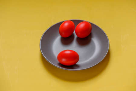 Colorful traditional painted Easter eggs. Red eggs, yellow background. Three eggs in a gray plateの写真素材
