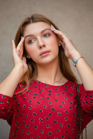 A girl in a red floral dress on a background of a beige wall. girl is young with natural long hair.の写真素材