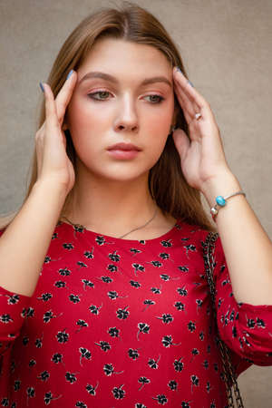 A girl in a red floral dress on a background of a beige wall. Vertical Portrait of a beautiful girの写真素材