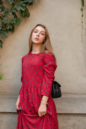 A girl in a red floral dress on a background of a beige wall. Vertical Portrait of a beautiful gir