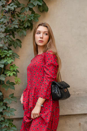 A girl in a red floral dress on a background of a beige wall. Vertical Portrait of a beautiful girの写真素材