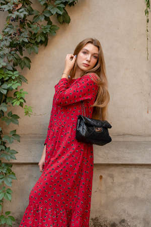 A girl in a red floral dress on a background of a beige wall. Vertical Portrait of a beautiful girの写真素材