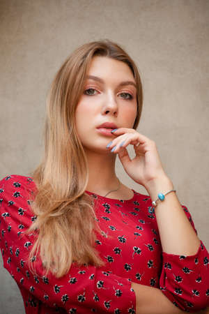 A girl in a red floral dress on a background of a beige wall. Vertical Portrait of a beautiful girの写真素材
