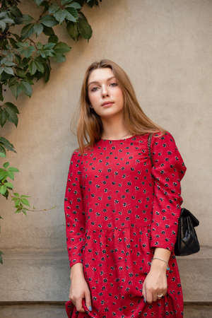 A girl in a red floral dress on a background of a beige wall. Vertical Portrait of a beautiful girの写真素材