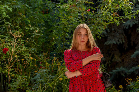 A girl in a red dress with long hair on a background of greenery in summer. beautiful girl in natureの写真素材