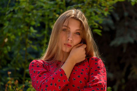 A girl in a red dress with long hair on a background of greenery in summer. beautiful girl in natureの写真素材