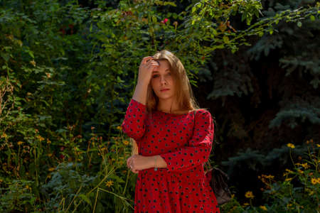 A girl in a red dress with long hair on a background of greenery in summer. beautiful girl in natureの写真素材