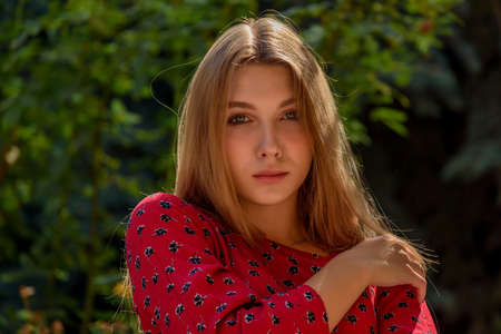 A girl in a red dress with long hair on a background of greenery in summer. beautiful girl in natureの写真素材