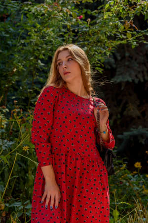 A girl in a red dress with long hair on a background of greenery in summer. beautiful girl in natureの写真素材