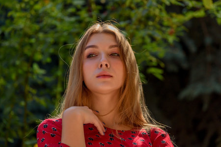 A girl in a red dress with long hair on a background of greenery in summer. beautiful girl in natureの写真素材