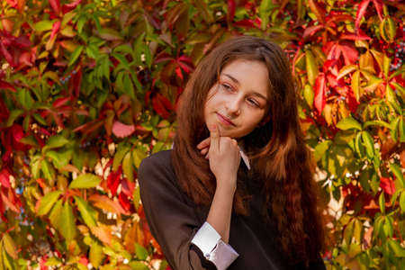 Girl 11 years old. Schoolgirl in school clothes in nature on a background of autumn leaves.の写真素材
