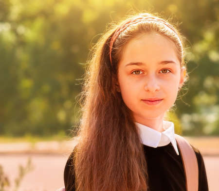Girl 11 years old. Schoolgirl in school clothes in nature on a background of leaves.の写真素材