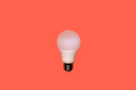 one white round type LED lamp with screw metal thread in the center on a red background, energy saving concept, copy spaceの写真素材
