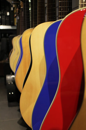 row close-up of red, blue and natural color classic acoustic guitar body in store