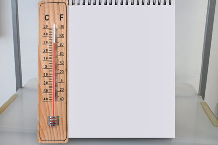 Celsius and Fahrenheit indoor wooden thermometer with an empty desk calendar or blank notepad on a...