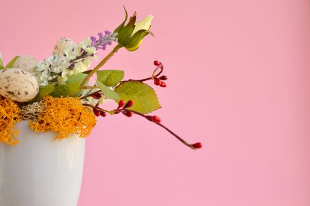 Easter composition of many artificial flowers and quail eggs in a white mug on a pink background, festive home decor, copy space for textの写真素材
