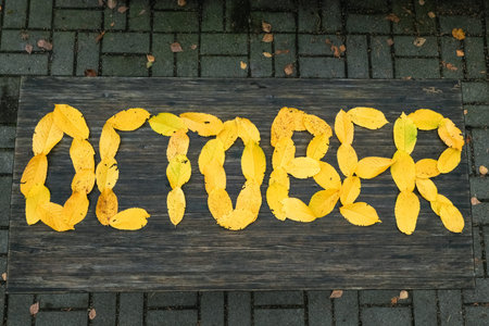 inscription October, handmade autumn composition of yellow leaves on a wooden table, top view