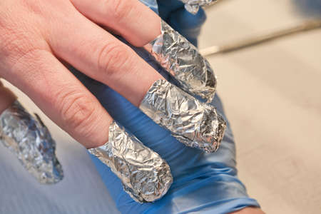 Foil on woman's nails during manicure. Fingernails covered with foil during the gel polish removal procedure.の写真素材