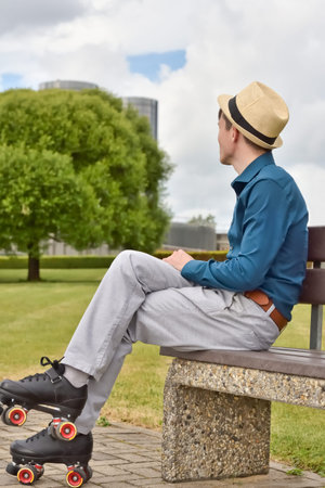 Young man in roller skates resting on a bench in a city park while skating in the city streets.