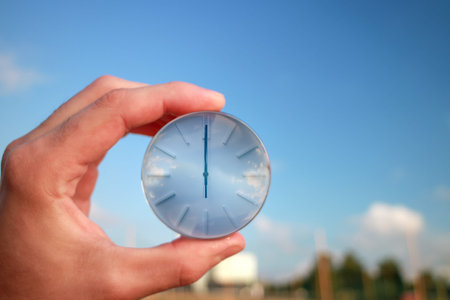 The dial of a watch in a hand against a background of blue sky. Twelve o'clock in the afternoon on...