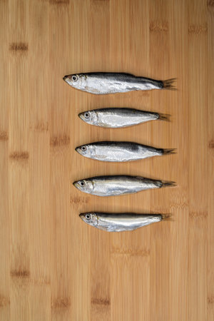 Fresh anchovies fish on wooden cutting board background. Raw fish prepared for cooking.の写真素材