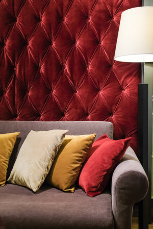 Sofa or couch with different colors cushions against red padded wall in classic style interior design living room for rest and loungeの写真素材