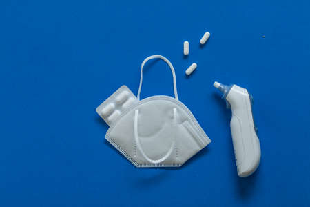 FFP3 mask, nasal drops, thermometer, tablets, various medicines lie on the table, top view, on a blue background, FlatLayの写真素材