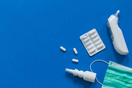 FFP3 mask, nasal drops, thermometer, tablets, various medicines lie on the table, top view, on a blue background, FlatLayの写真素材