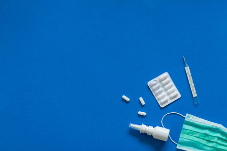 FFP3 mask, nasal drops, thermometer, tablets, various medicines lie on the table, top view, on a...