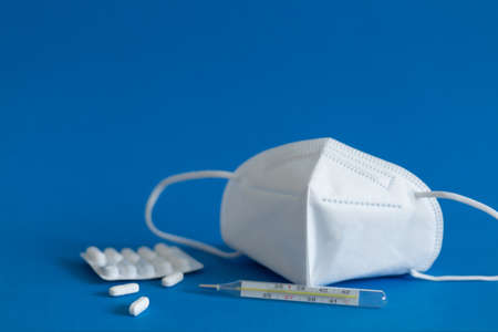 FFP3 mask, nasal drops, thermometer, tablets, various medicines lie on the table, top view, on a blue background, FlatLayの写真素材