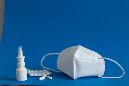 FFP3 mask, nasal drops, thermometer, tablets, various medicines lie on the table, top view, on a blue background, FlatLayの写真素材